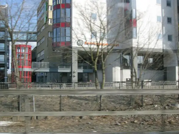 Modern byggnader med glasfasader och en röd, cylindrisk hiss. Skylten "Kunskapsgymnasiet Globen" syns på en av byggnaderna.