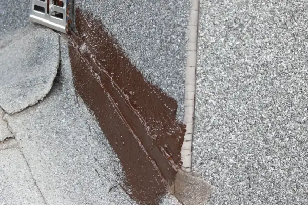 Brązowy lepik uszczelnia dach. Widać metalowy element odpływu.