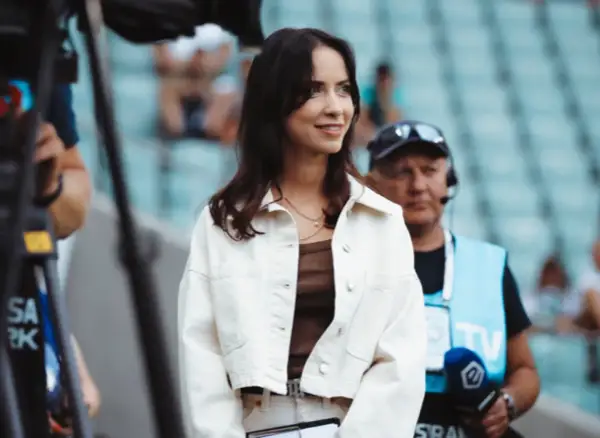 Maja Strzelczyk w białej kurtce, gotowa do pracy na stadionie. W tle widać ekipę telewizyjną.