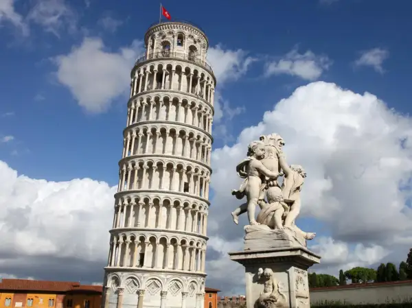 La Torre Pendente di Pisa, con la sua inconfondibile inclinazione, si erge maestosa sotto un cielo azzurro e nuvoloso, accanto a una scultura di putti.