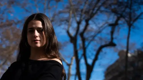 Elvira Lara, una joven con cabello castaño, mira a la cámara con un fondo de árboles y cielo azul.