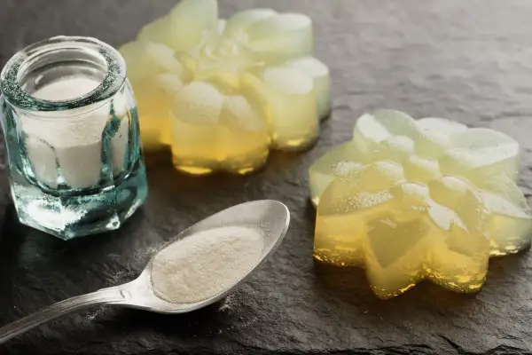 Proszek agar w słoiczku i na łyżce, obok galaretki w kształcie kwiatów. Agar to naturalny środek żelujący.