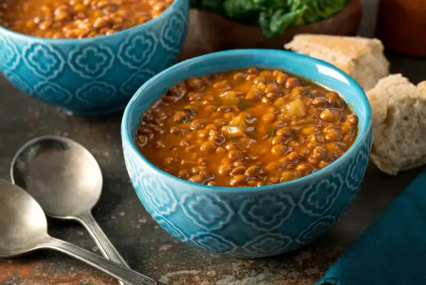 Bol de soupe de lentilles savoureuse, une recette réconfortante avec du pain et des couverts.