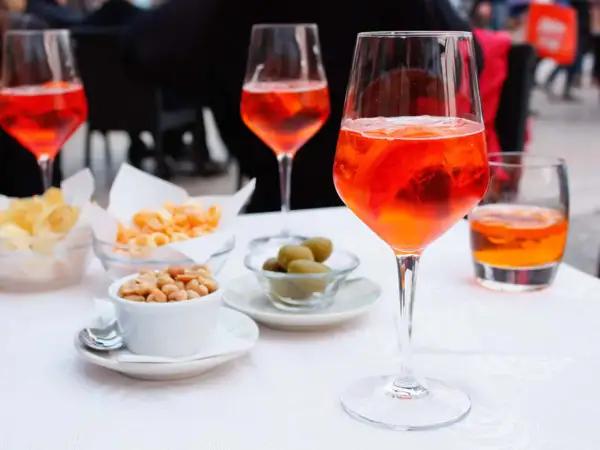 En aperitivo betyder njutning före maten. Här syns Aperol Spritz med snacks som nötter, oliver och chips.