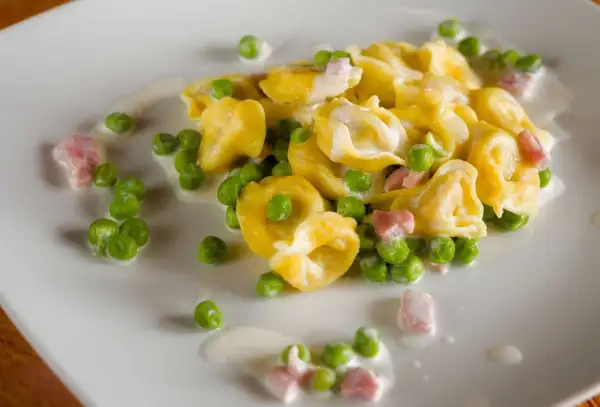 Tortellini di carne con piselli e pancetta, un classico condimento per un primo piatto gustoso e cremoso.