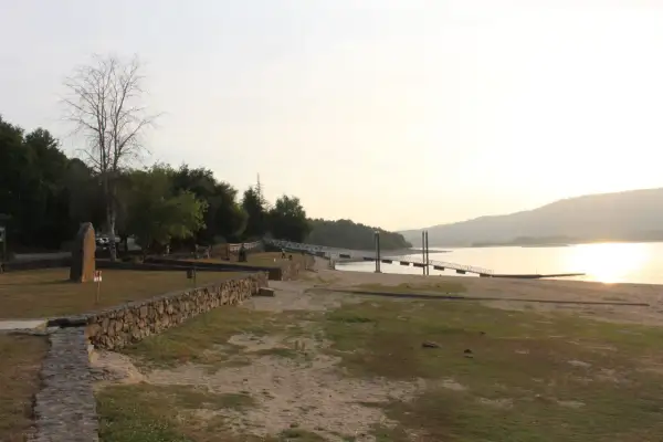 Un tranquilo atardecer en la playa fluvial o corgo, con un muelle y vegetación verde.