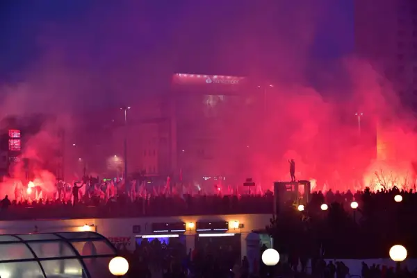 Tłum z polskimi flagami, race i dym tworzą atmosferę manifestacji. W tle widać budynki i billboard Santander. To obraz silnego nacjonalizmu.