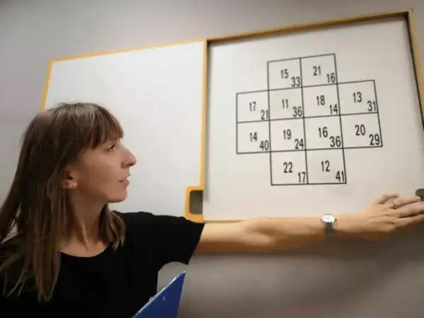 Kobieta przeprowadza testy psychologiczne dla kierowców, wskazując na tablicę z liczbami.