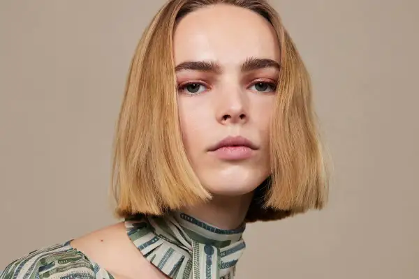 Modelka z idealnie prostymi, rudymi włosami w stylu blunt bob, z delikatnym makijażem oczu i ust, prezentuje się elegancko.