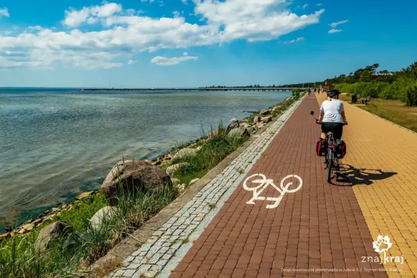 Kobieta na rowerze przemierza malowniczą trasę rowerową Władysławowo Hel. Widok na morze i molo.