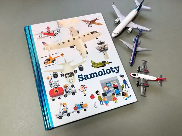Książki o samolotach z ilustracjami różnych maszyn latających i ludzi pracujących na lotnisku. Obok leżą modele samolotów.