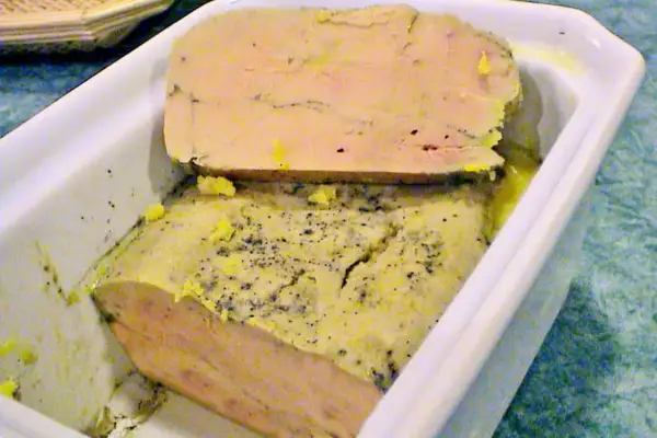 Un délice à partager : un foie gras mi cuit en terrine, parsemé de poivre, prêt à être dégusté.