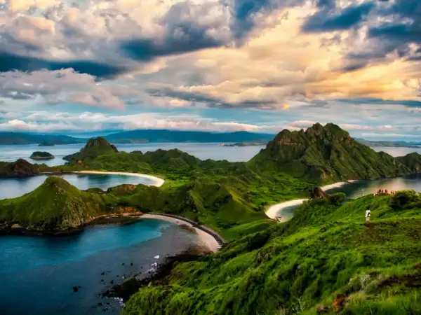 Grüne Hügel und weiße Sandstrände im Komodo Nationalpark, Indonesien. Ein einsamer Wanderer genießt die atemberaubende Aussicht auf das Meer.