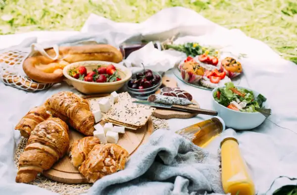 Pyszne jedzenie na piknik: świeże croissanty, bagietka, truskawki, wiśnie, sałatka, kiełbasa i napoje.
