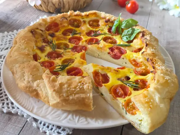 Une quiche ricotta aux tomates cerises et romarin, garnie de graines de sésame, sur une assiette blanche.
