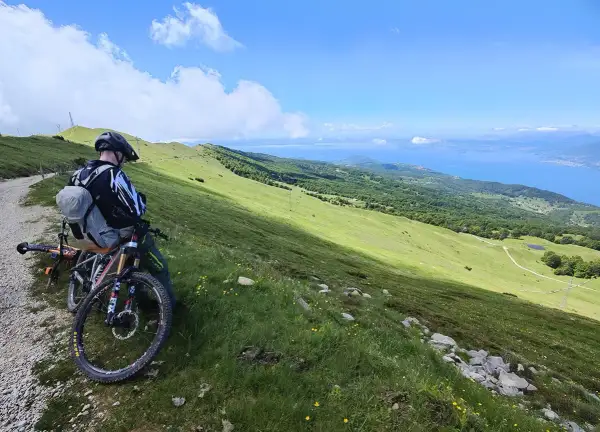 Ciclista con mountain bike ammira il panorama del lago di Garda dal Monte Baldo.