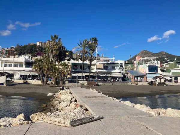 Paseo marítimo en la playa pedregalejo como llegar. Palmeras, restaurantes y montañas al fondo bajo un cielo azul.