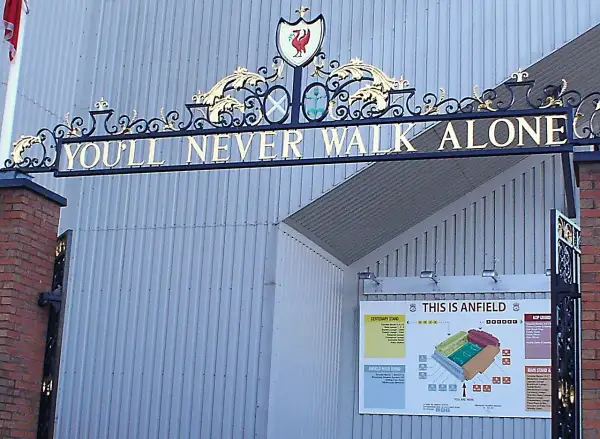 L'iconico cancello di Anfield con la scritta "You'll Never Walk Alone" e lo stemma del Liverpool. Un simbolo di unità e passione.