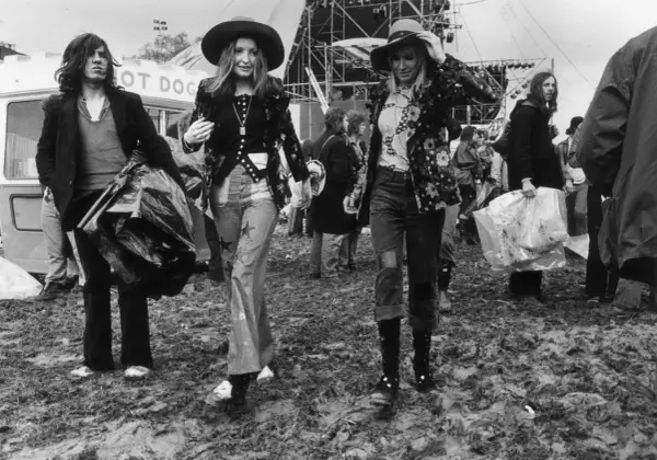 Moda hipisowska lat 70. na festiwalu. Dwie kobiety w kapeluszach i kwiecistych kurtkach, mężczyzna z torbą.