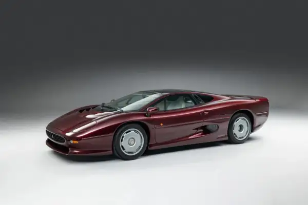 Bordowy Jaguar XJ220, ikona lat 90., prezentuje swoje aerodynamiczne linie na tle szarego studia.