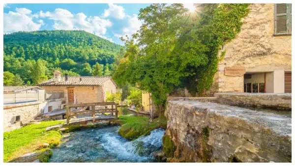 Un ruscello attraversa un borgo umbro con case in pietra e vegetazione lussureggiante. Una cartina ideale per scoprire i borghi dell'Umbria.