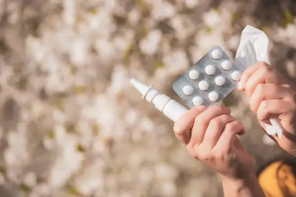 Ręce trzymające spray do nosa, tabletki i chusteczkę, gotowe na walkę z alergią.