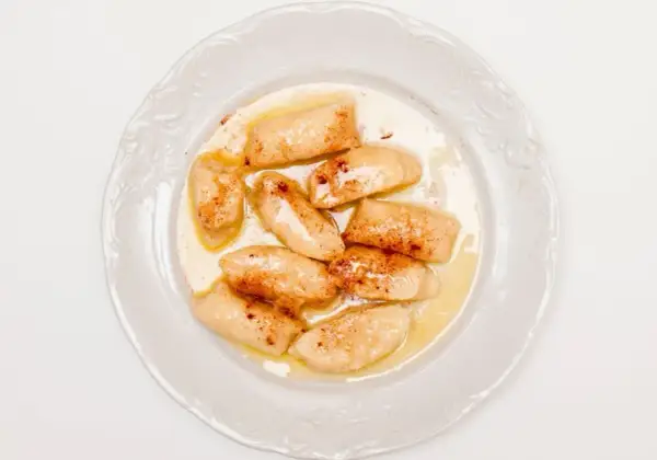 Pyszne pierogi leniwe bez ziemniaków, polane masłem i posypane cynamonem, na białym talerzu.