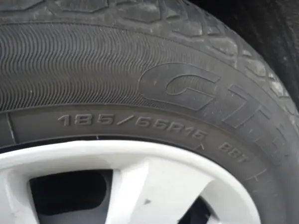 Gros plan sur un pneu rechapé avec inscription 185/65R15. La jante est visible en bas.
