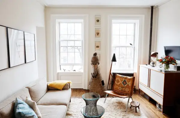 A bright living room with a sofa, fluffy rug, and two windows, demonstrating how to make a small space feel large with light and airy decor.