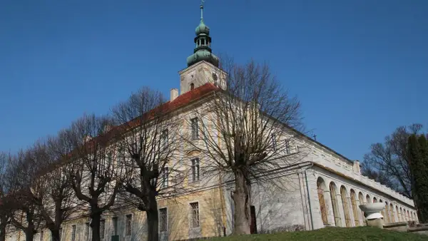 Dawny pałac w Oleśnicy Małej z charakterystyczną wieżą i arkadowym krużgankiem, otoczony nagimi drzewami.