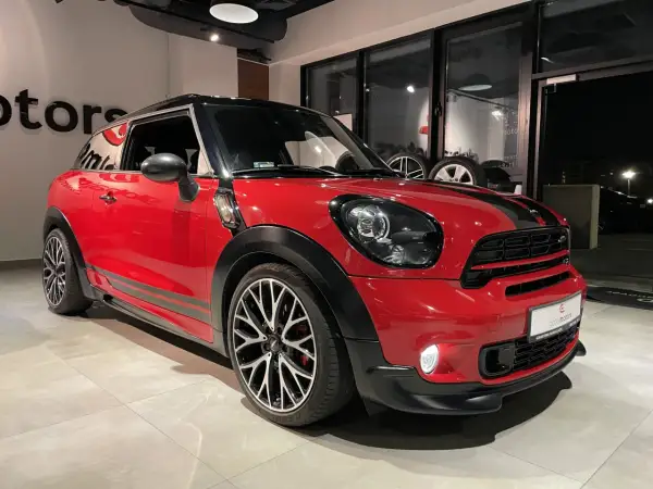 Czerwony mini paceman z czarnymi pasami i felgami stoi w salonie.