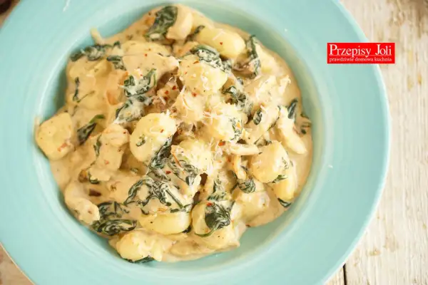 Pyszne gnocchi z kurczakiem w sosie śmietanowym, ze szpinakiem i parmezanem, podane na turkusowym talerzu.