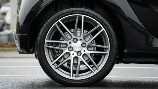 Błyszczące, czarne nadkole samochodu z felgą Brabus i oponą na mokrej nawierzchni.