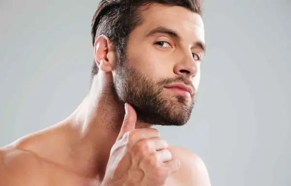 Un homme au regard intense, sa main effleurant sa barbe bien taillée. Une coupe barbe homme parfaite pour un style affirmé.