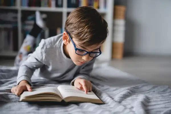 Niño con gafas azules concentrado en un libro abierto, aprendiendo a leer.