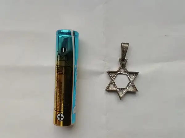 Obok baterii AAA leży srebrny wisiorek w kształcie Gwiazdy Dawida. To symbol, co oznacza przynależność i tożsamość.