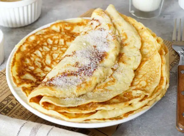 Ein Stapel goldbrauner Pfannkuchen, bestreut mit Zucker. Ein einfaches Pfannkuchen Rezept für jeden Tag.