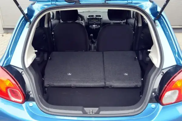 Błękitny Mitsubishi Space Star z otwartym bagażnikiem. Widoczne złożone tylne siedzenia, tworzące płaską przestrzeń ładunkową.