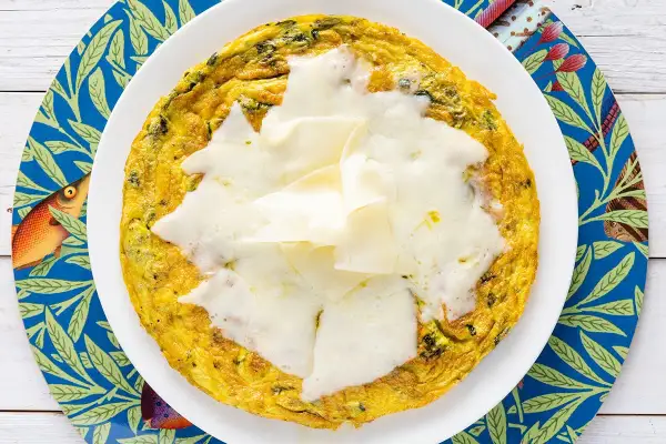 Frittata di bietole dorata e filante, servita su un piatto bianco con un sottobicchiere blu decorato con pesci e foglie.