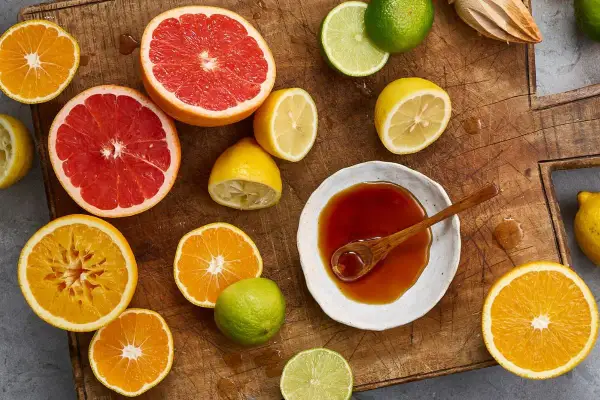 Färska citrusfrukter som apelsiner, grapefrukt och citroner, samt en skål med mörk vätska, antyder ingredienser för ett ponzu recept.