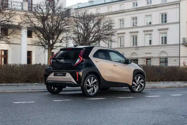 Dwukolorowy Toyota Aygo X na ulicy, z tyłu widoczny budynek z kolumnami.