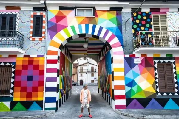 Un uomo in piedi sotto un arco colorato, un'esplosione di arte urbana che celebra l'Italia, patria della bellezza.