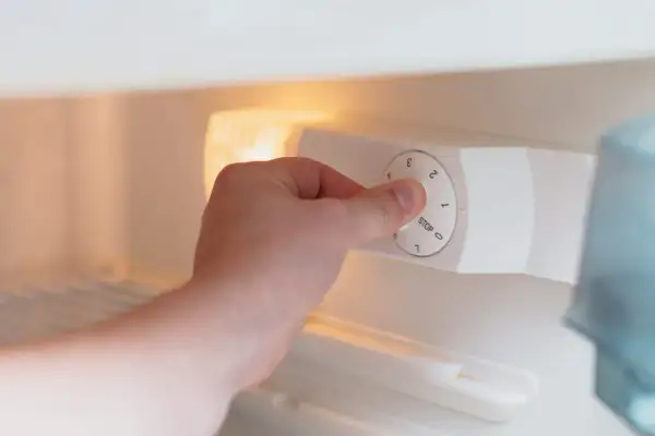 Main tenant ajuste la température d'un frigo. Le bouton est réglé sur 1, juste au-dessus de "STOP".