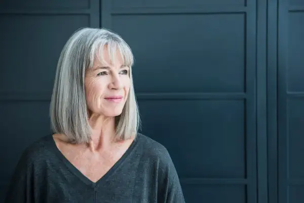 Een vrouw met grijs haar kijkt peinzend weg. Ze straalt een rustige kracht uit, wat kan passen bij de complexiteit van autisme bij vrouwen.