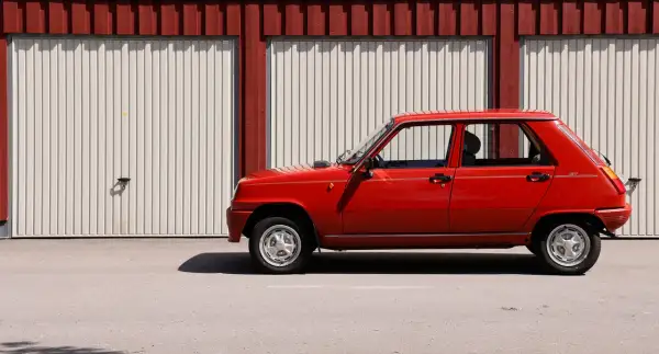 Röd Renault 5 GL står parkerad framför en röd och vit garagebyggnad. Denna klassiska le car är redo för en tur.