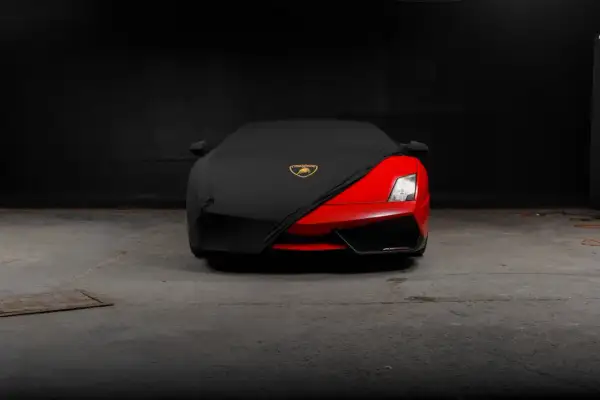 Czerwony supersamochód Lamborghini, być może najdroższe auto na świecie, częściowo przykryty czarnym pokrowcem z logo marki.