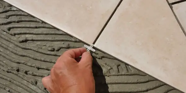 Pose de carrelage en cours, une main place un croisillon. Le prix pose carrelage m2 dépend de la complexité.