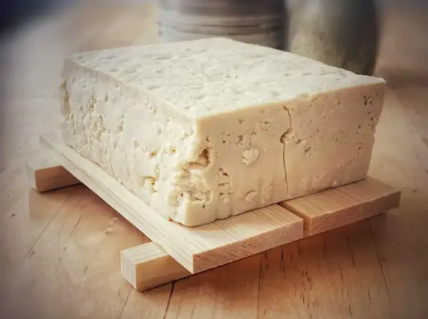 Duży blok domowego, białego tofu na drewnianej podstawce.