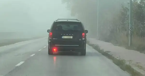 Ciemny van Dodge jedzie we mgle, włączone światła przeciwmgielne tylne poprawiają widoczność.