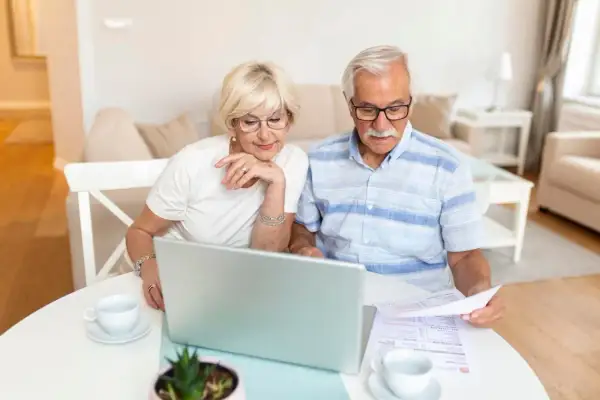 Para seniorów analizuje dokumenty przy laptopie, zastanawiając się, czy emeryci częściej wygrywają w loteriach pożyczkowych skierowanych do seniorów.